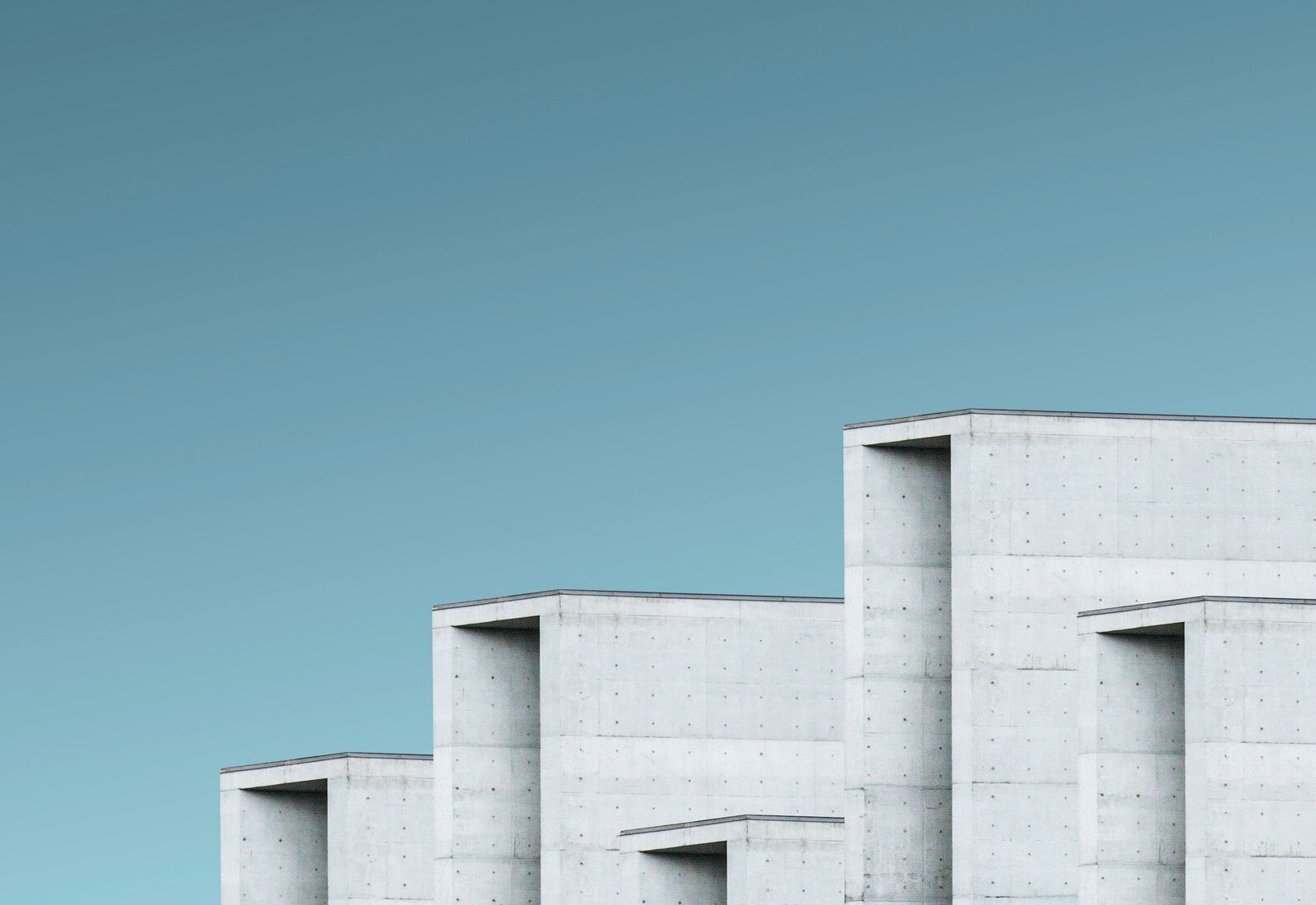 Concrete forms stepping in a row against a clear teal sky, seen from below.