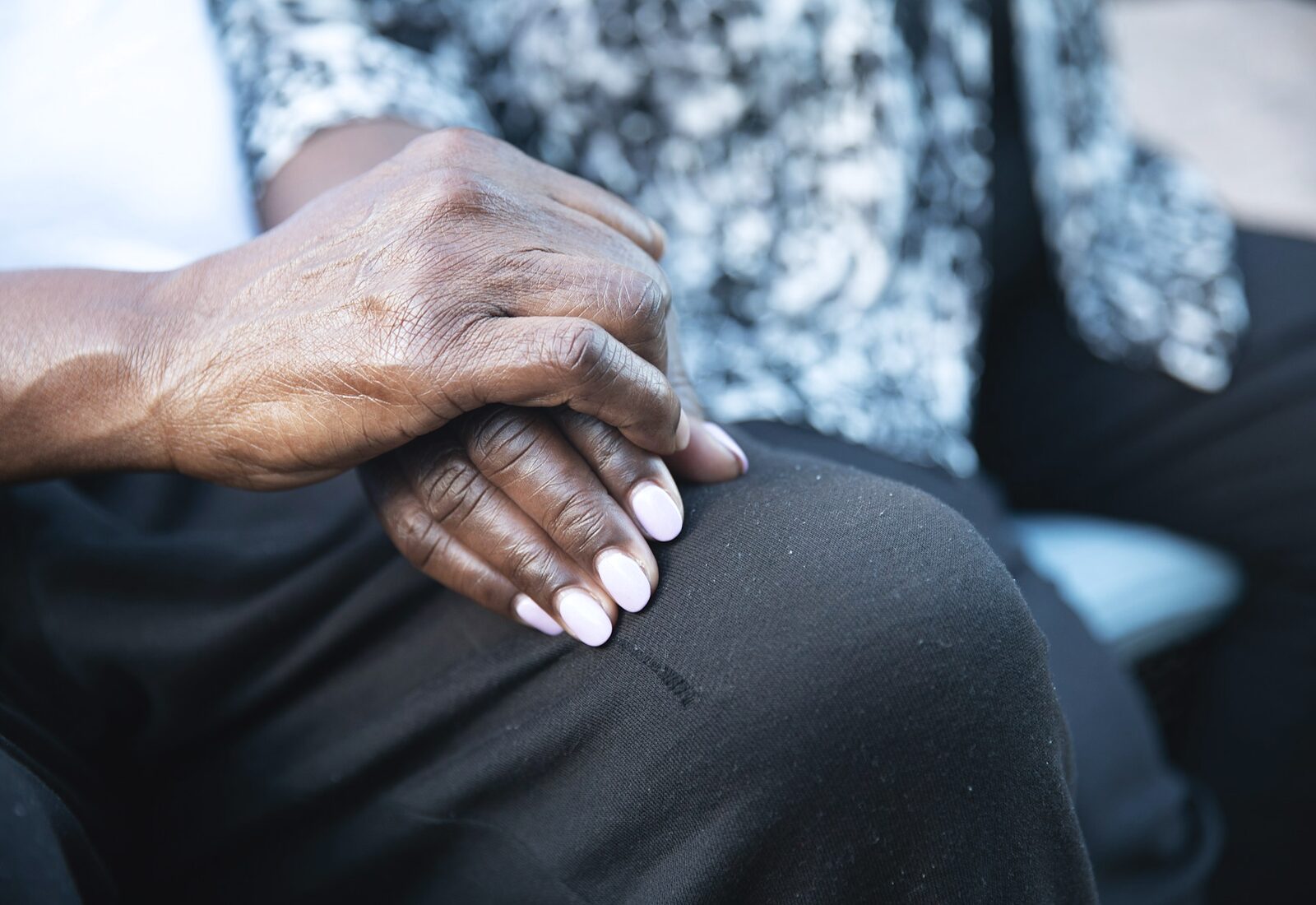 Close-up of an older person's hand resting on a younger person's hand, folded quietly in a lap.