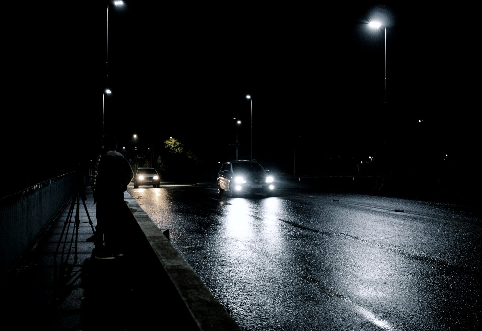 Headlights on a rain-slicked road at night, streetlights streaking across the wet asphalt.